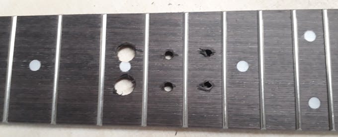 Fretboard, front side, with 4 nicely (d~ 2mm) and 2 badly (="too deep", therfore too large diam) drilled holes.