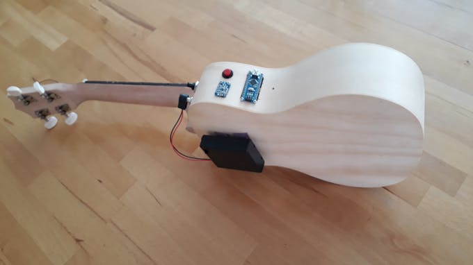 Rear view, showing battery pack attached to the ukulele's body by hook-and-loop-fastener.