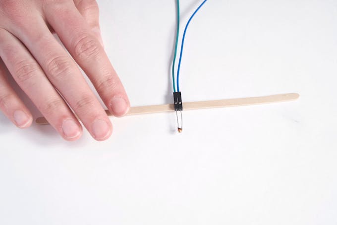Insert the leads of the first thermistor into female-ended jumper wires, then glue to stir stick