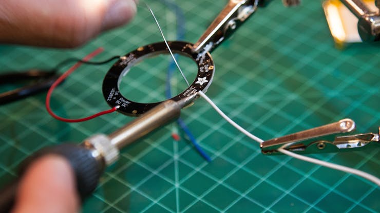 Cut three wires to a length of 2 inches, strip the ends, and solder to V+ , G and IN on the NeoPixel ring. (See Flora to NeoPixels Wiring Diagram in the Schematics section.)