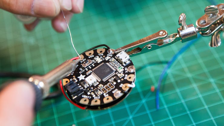 Place the Neopixel ring on the back of the Flora and solder the appropriate wires to 3.3V , GND and Pin9. (See Flora to NeoPixels Wiring Diagram in the Schematics section.)